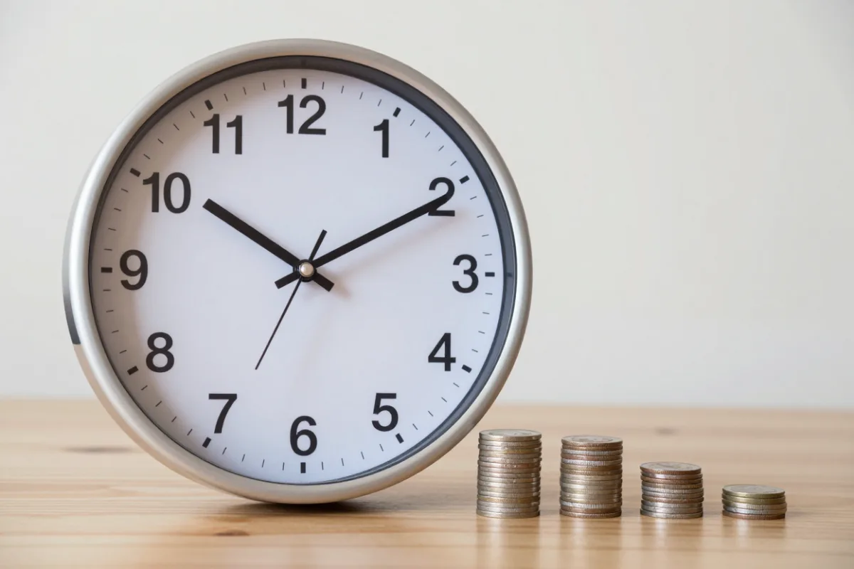 A clock beside growing stacks of coins, showing savings growing over time