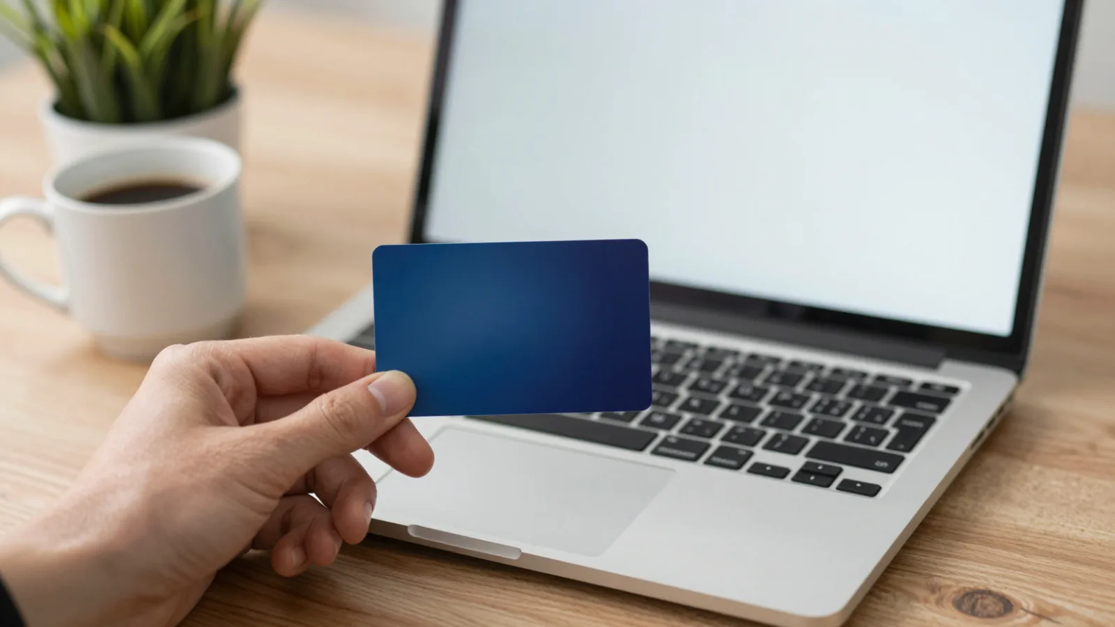 A hand holding a credit card beside a laptop