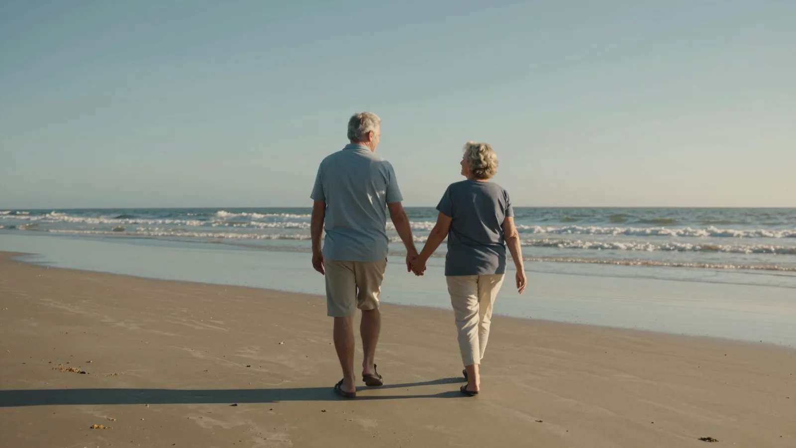 An older couple walking along a beach at sunset